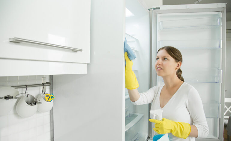 En flicka rengör ett kylskåp i rostfritt stål.