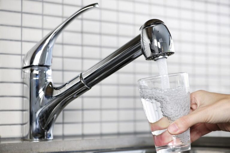 häller vatten i ett glas från kranen