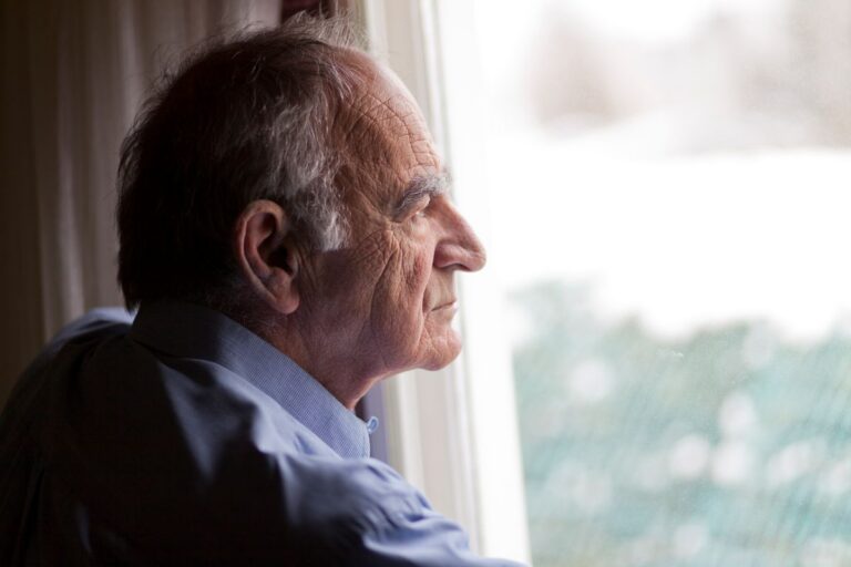En 60 år man tittar sorgset ut genom fönstret.