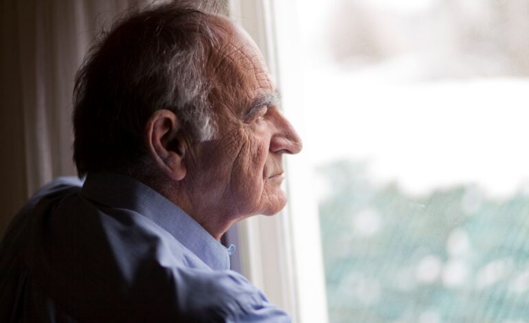 En 60 år man tittar sorgset ut genom fönstret.