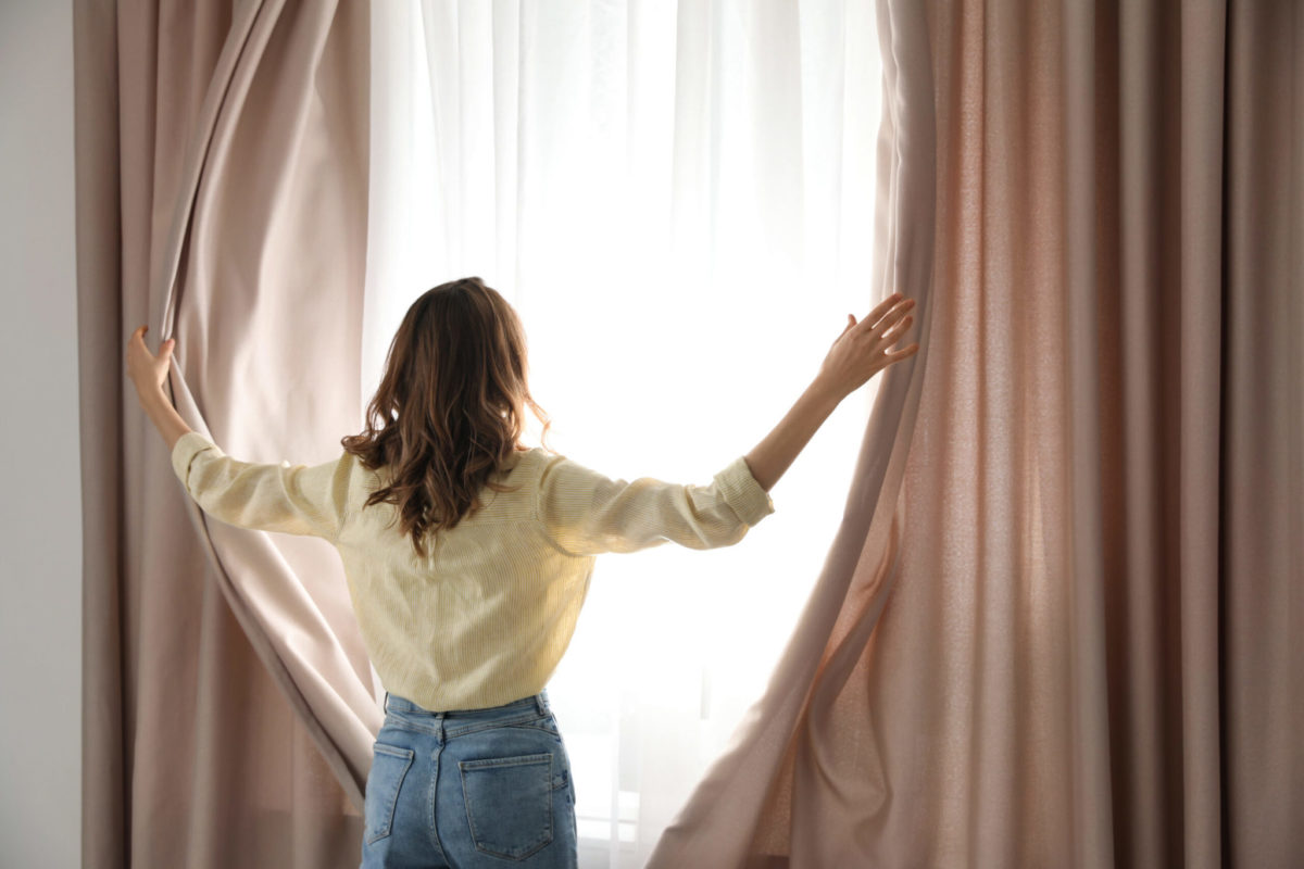 En kvinna drar undan gardinerna.