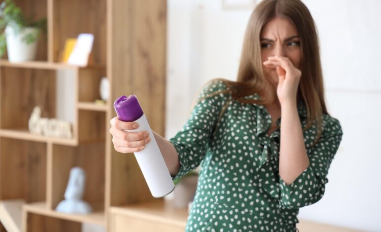 täcker näsan med handen för att blockera den obehagliga lukten och sprutar luftfräschare för att dölja lukten i badrum
