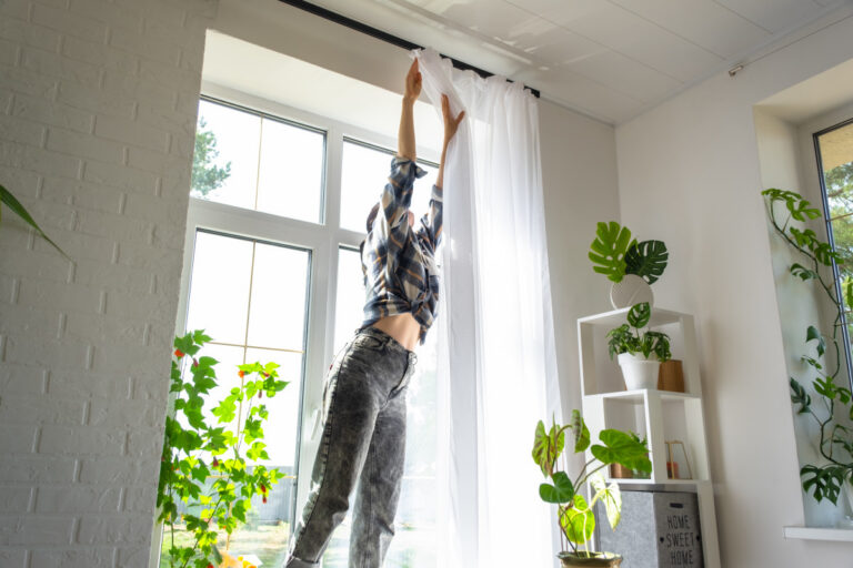 En kvinna tar ner gardinerna från gardinstången.